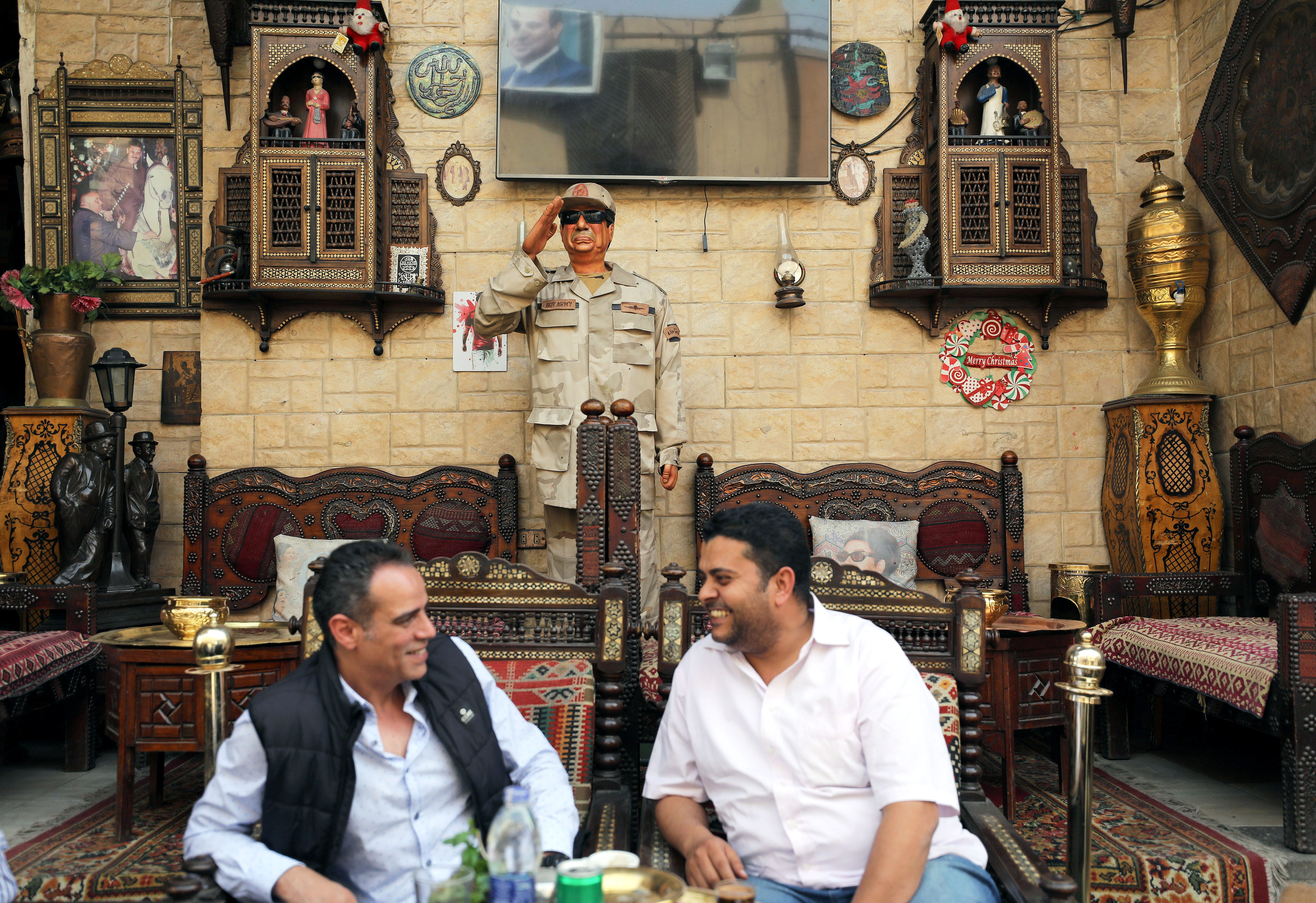 مصريون يجلسون في أحد مقاهى القاهرة أمام تمثال للرئيس المصري عبد الفتاح السيسي/ رويترز