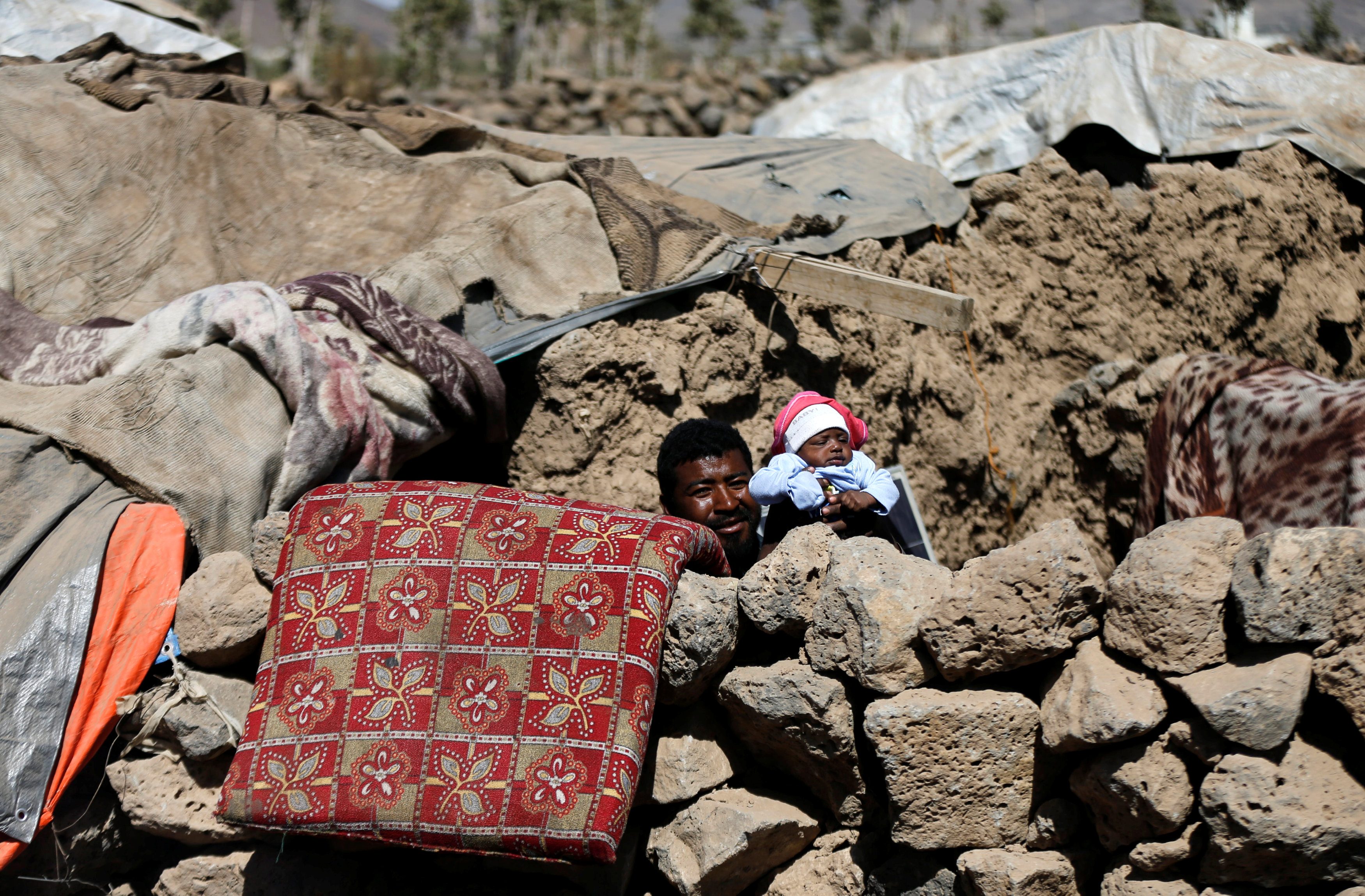 رجل يحمل طفله المولود حديثًا بالقرب من كوخه في مخيم مؤقت للنازحين قرب صنعاء ، اليمن