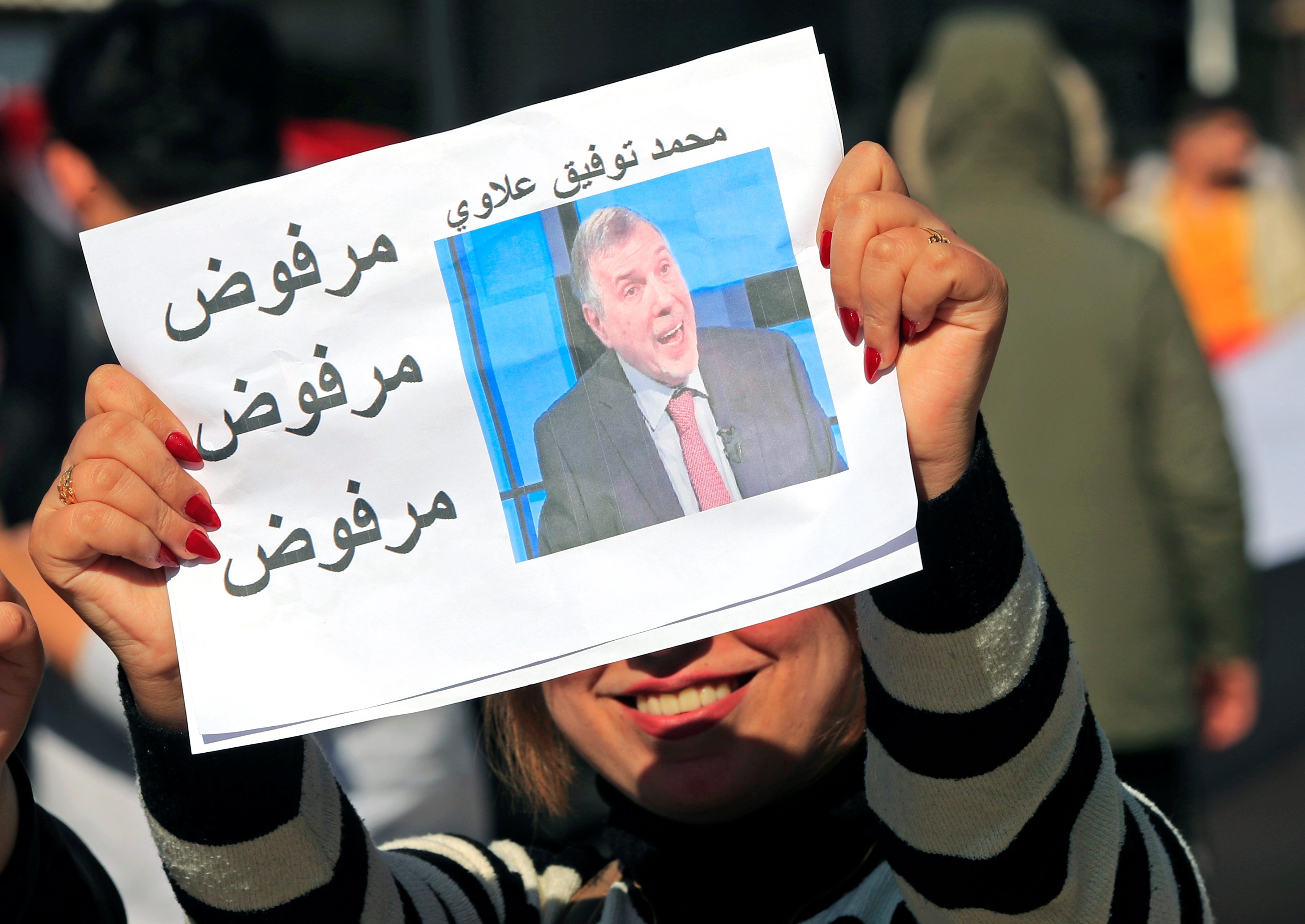 طالبة جامعية عراقية تحمل لافتة مع صورة رئيس الوزراء العراقي المعين حديثًا ، محمد توفيق علاوي ، للتعبير عن رفضها له