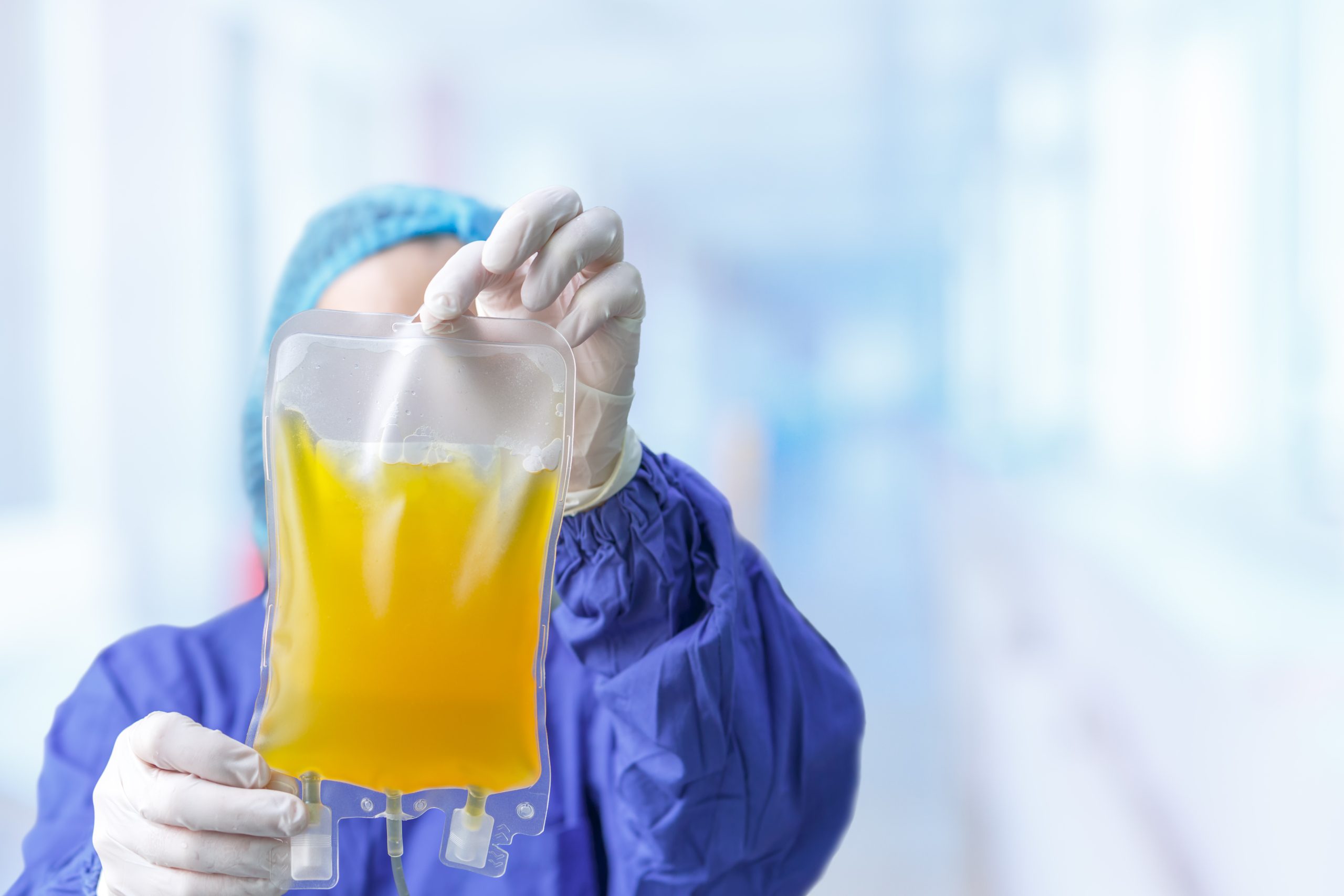Gloved hands of a medical professional holding a bag of blood plasma close-up.