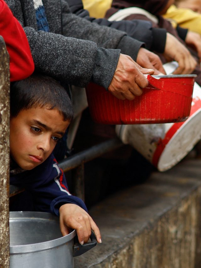 Palestinian children wait to receive food cooked by a charity kitchen amid shortages of food supplies, in Rafah