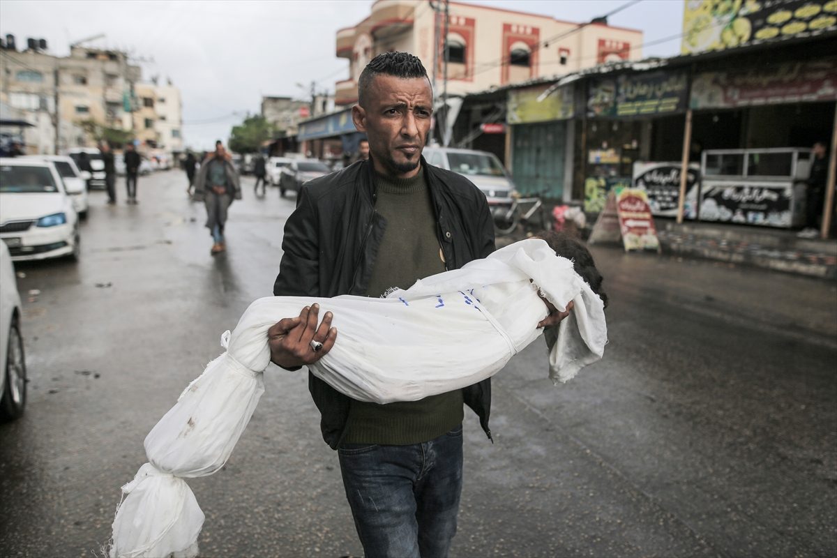 فلسطيني يحمل جثمان طفل فلسطيني استشهد بعد قصف الاحتلال لمنازل في رفح/الأناضول